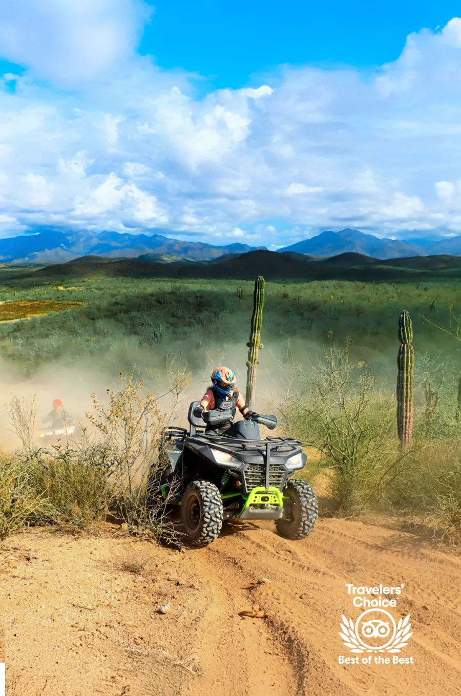 ATV rider on a dusty desert trail surrounded by cacti, mountains in the background, with a Travelers' Choice badge displayed.