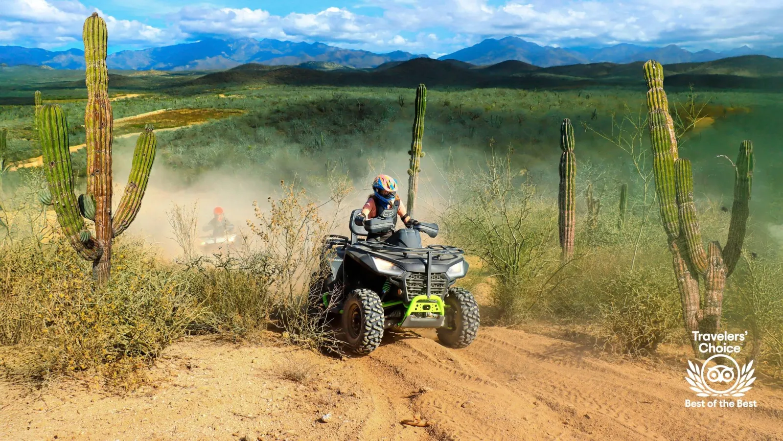 ATV rider on a dusty desert trail surrounded by cacti, mountains in the background, with a Travelers' Choice badge displayed.